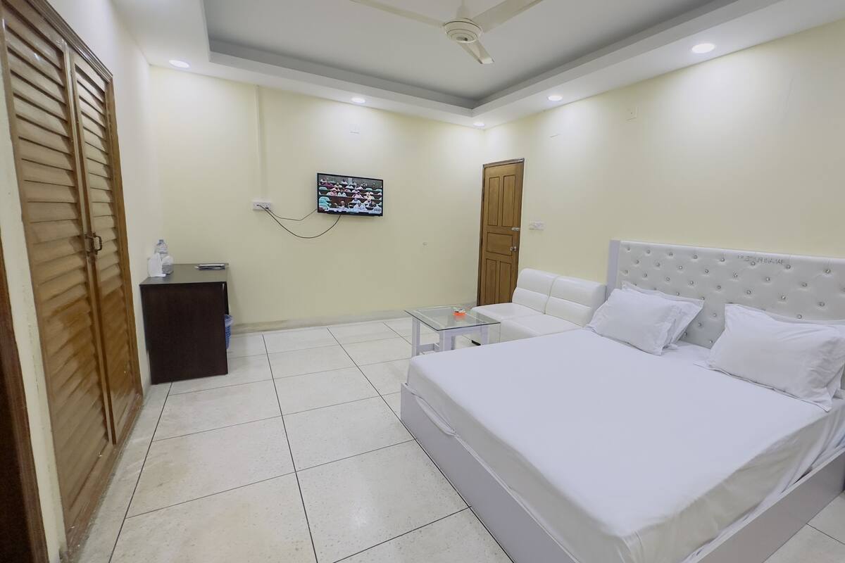 A bedroom with a large bed, a bedside table, a TV mounted on the wall, and a wooden door.