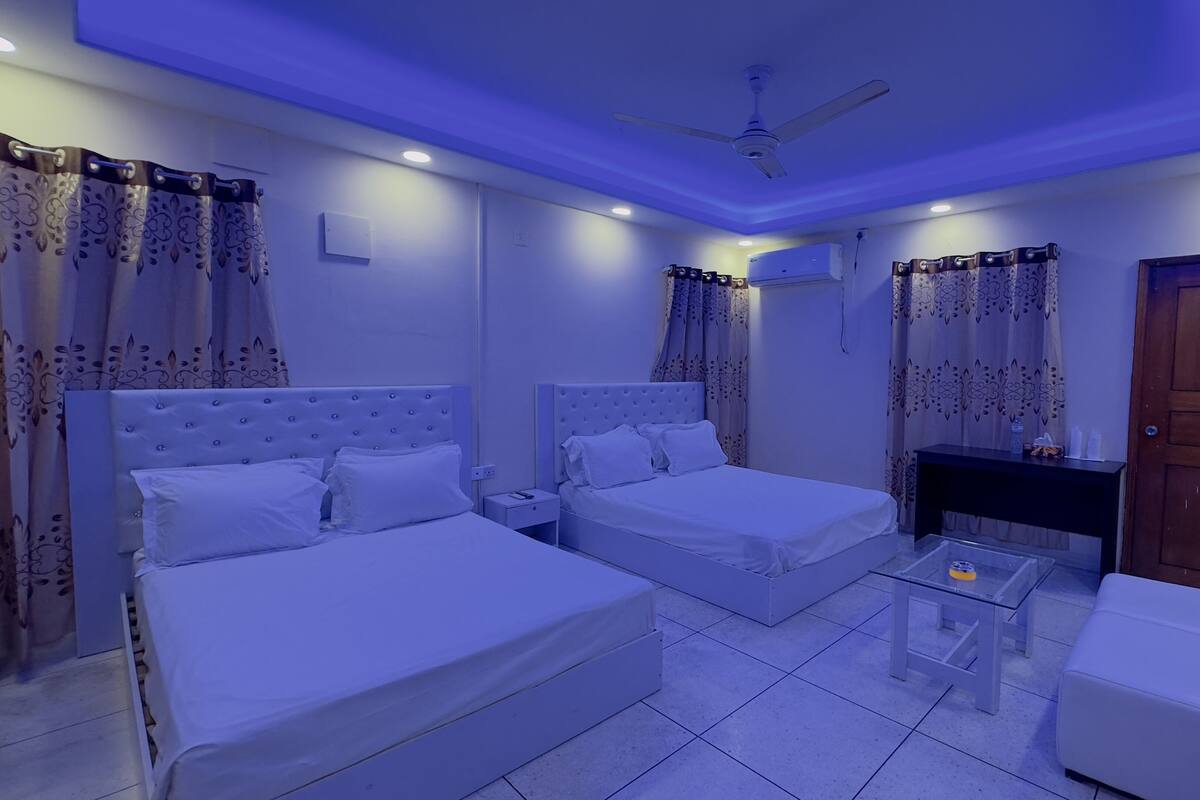 A hotel room with two beds, a ceiling fan, a TV, and a small table.