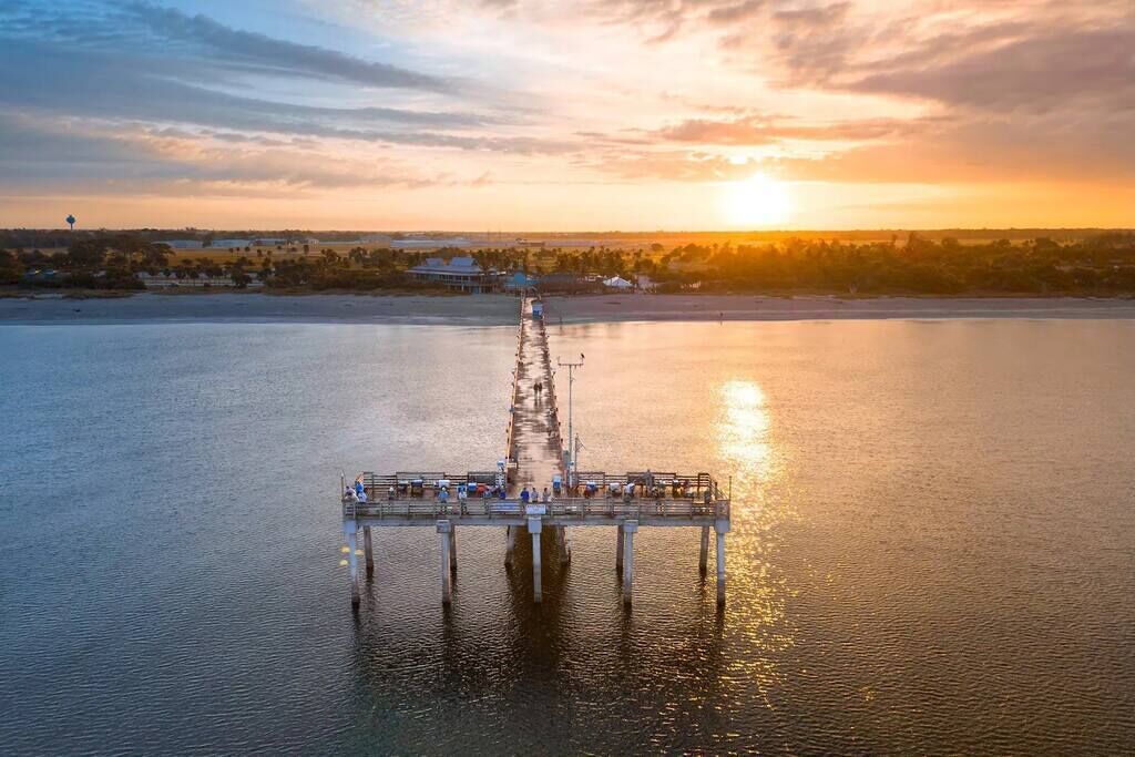 En mole, der strækker sig ud i roligt vand, med en solnedgang i baggrunden.