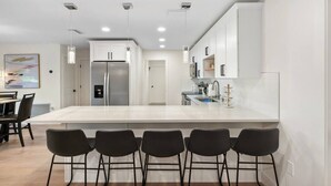 A modern kitchen with a large island, bar stools, and pendant lighting.