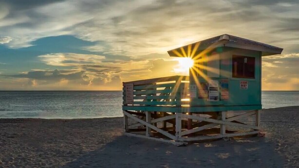 A lifeguard tower on a beach with the sun setting in the background.