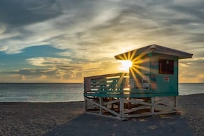 A lifeguard tower on a beach with the sun setting in the background.