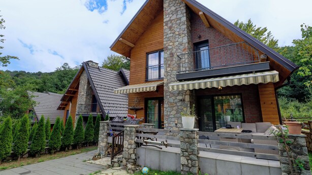 Une maison moderne avec une façade en pierre, des poutres en bois et un balcon.