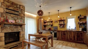 Une cuisine chaleureuse avec une cheminée en pierre, une table à manger en bois et des luminaires suspendus.