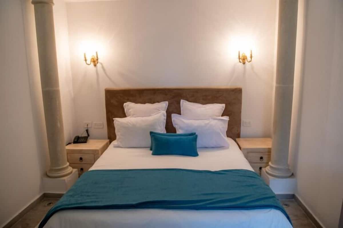 A hotel room with a large bed, two bedside lamps, and a nightstand with a phone.