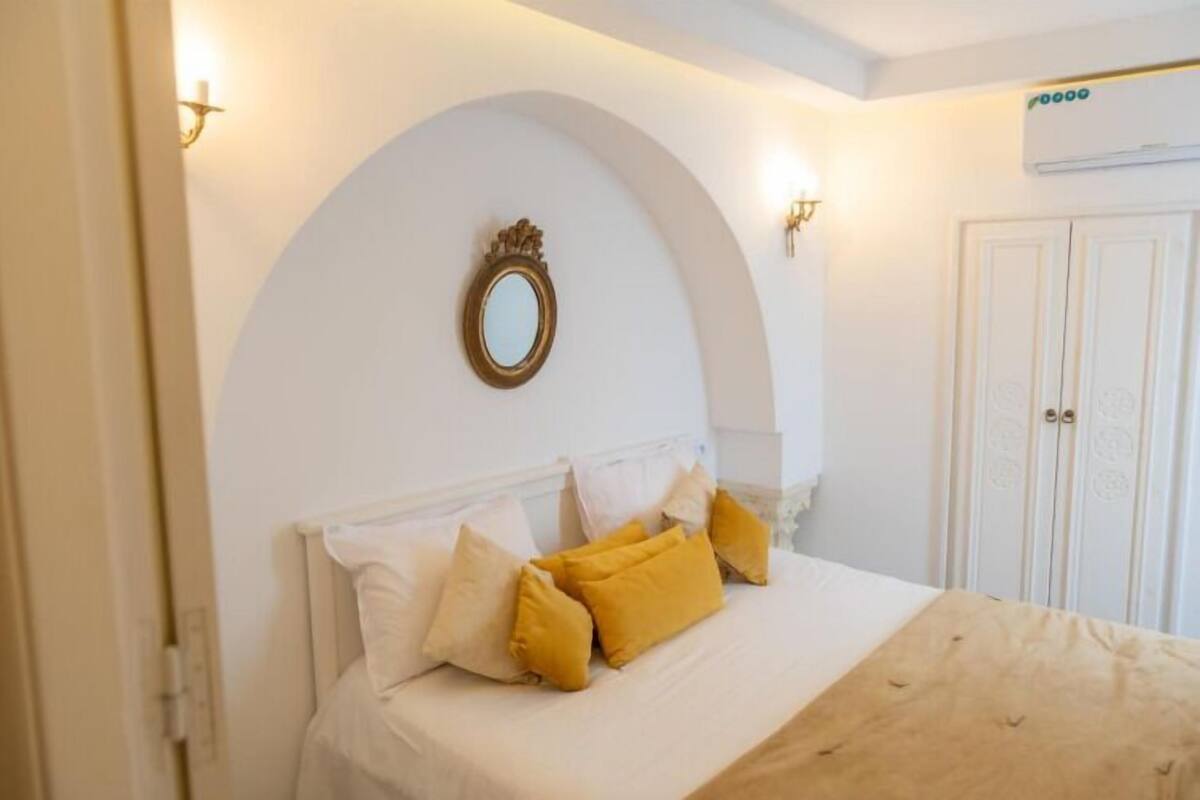 A bedroom with a bed, white walls, a mirror, and a wardrobe.