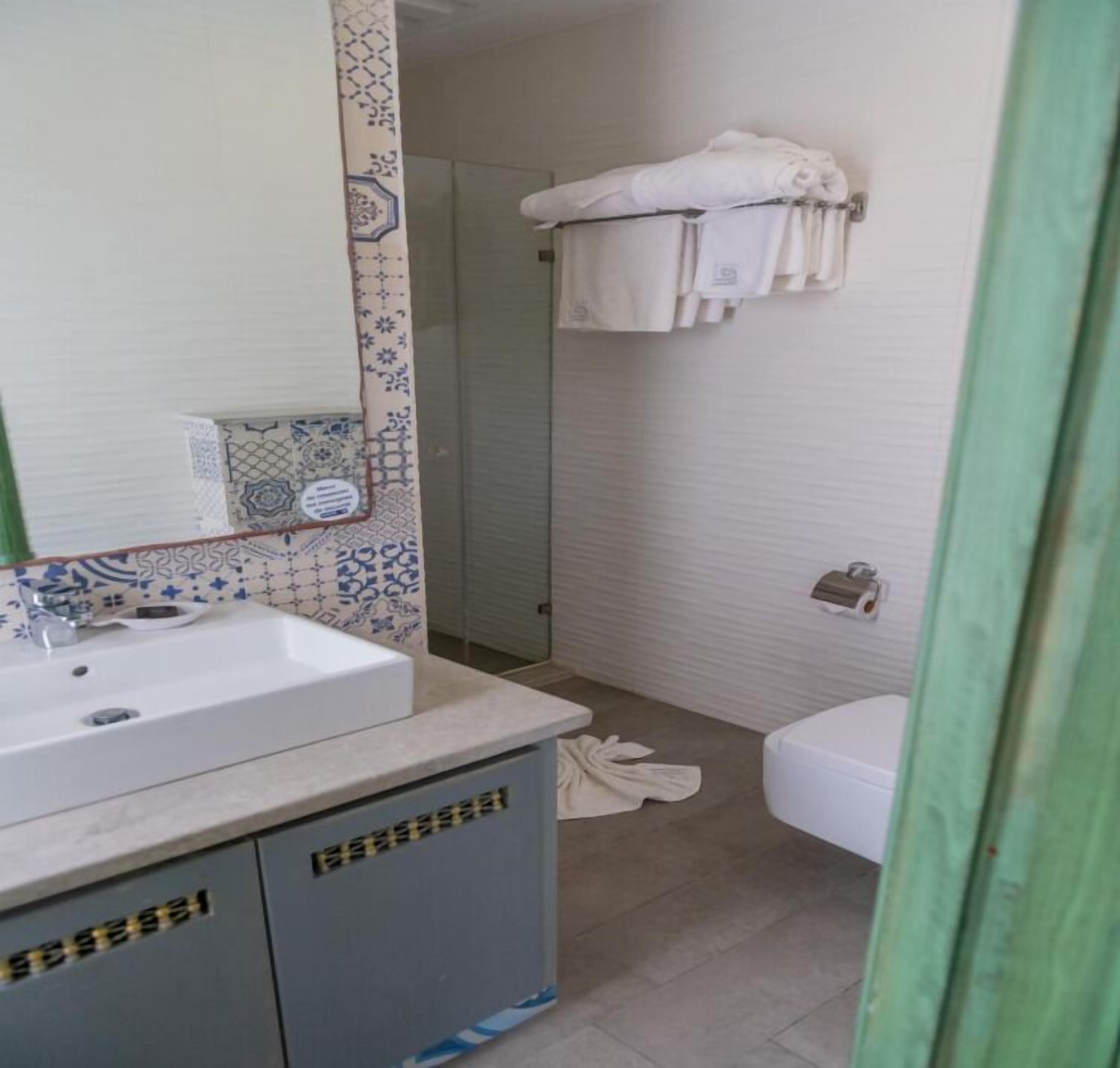 Une salle de bain avec un lavabo blanc, un miroir, des carreaux décorés, un porte-serviettes et des toilettes.