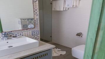 Une salle de bain avec un lavabo blanc, un miroir, des carreaux décorés, un porte-serviettes et des toilettes.
