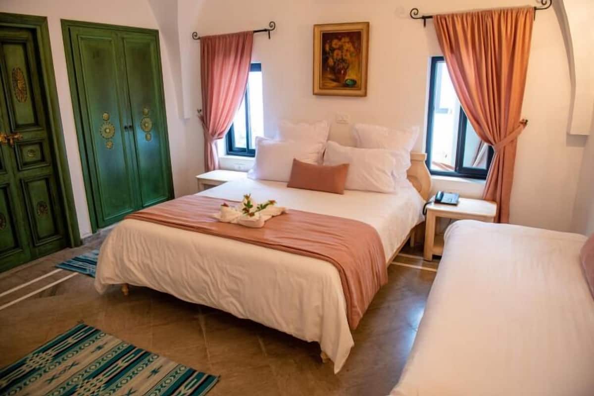A bedroom with a large bed, two bedside tables, a window with curtains, and a green door.