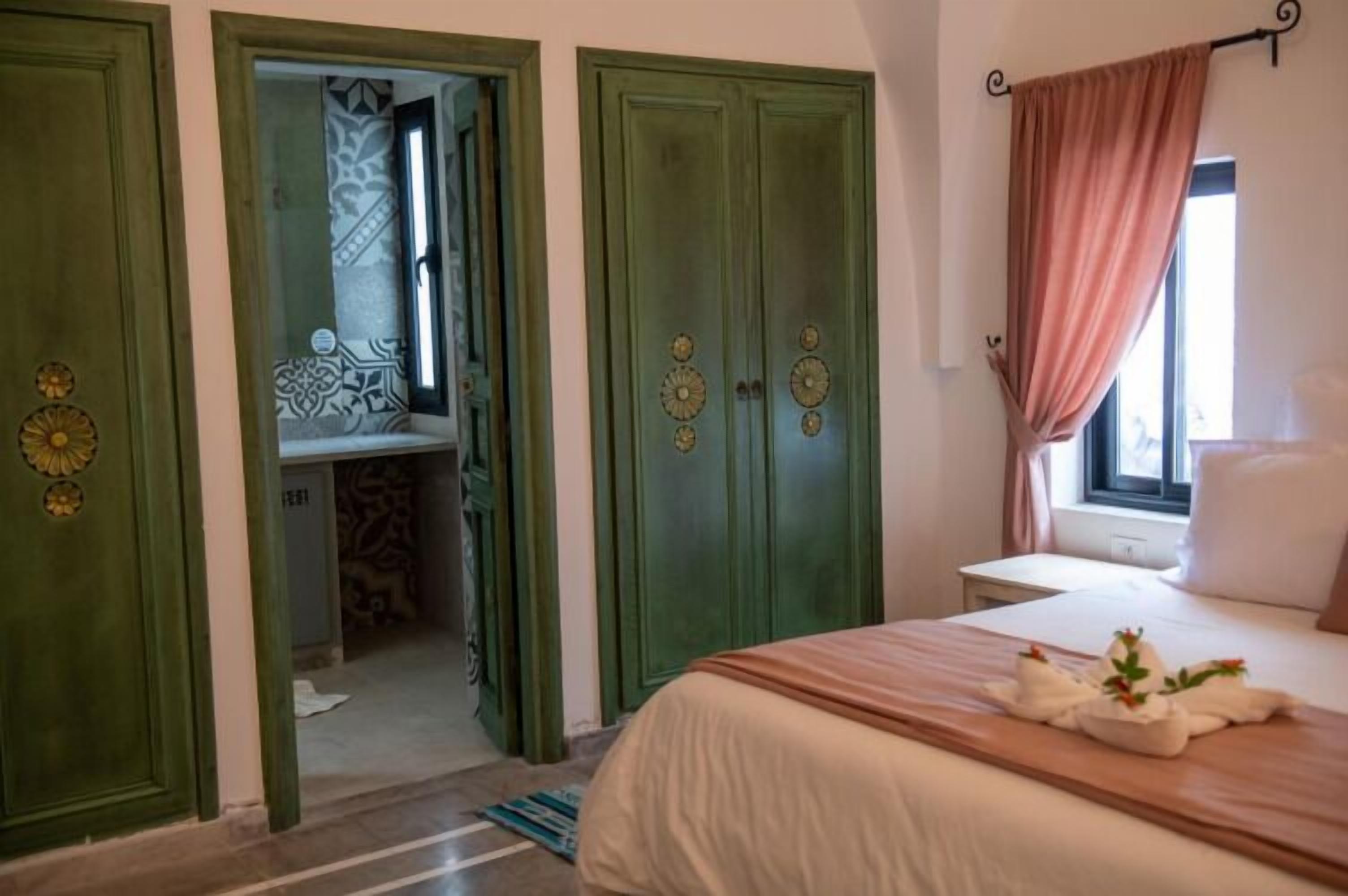 Une chambre à coucher avec un lit, une fenêtre avec des rideaux et une porte donnant sur une salle de bain.