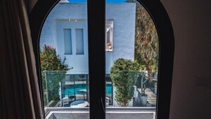 A view through a double door with a clear sky, a pool, and a building with shutters.