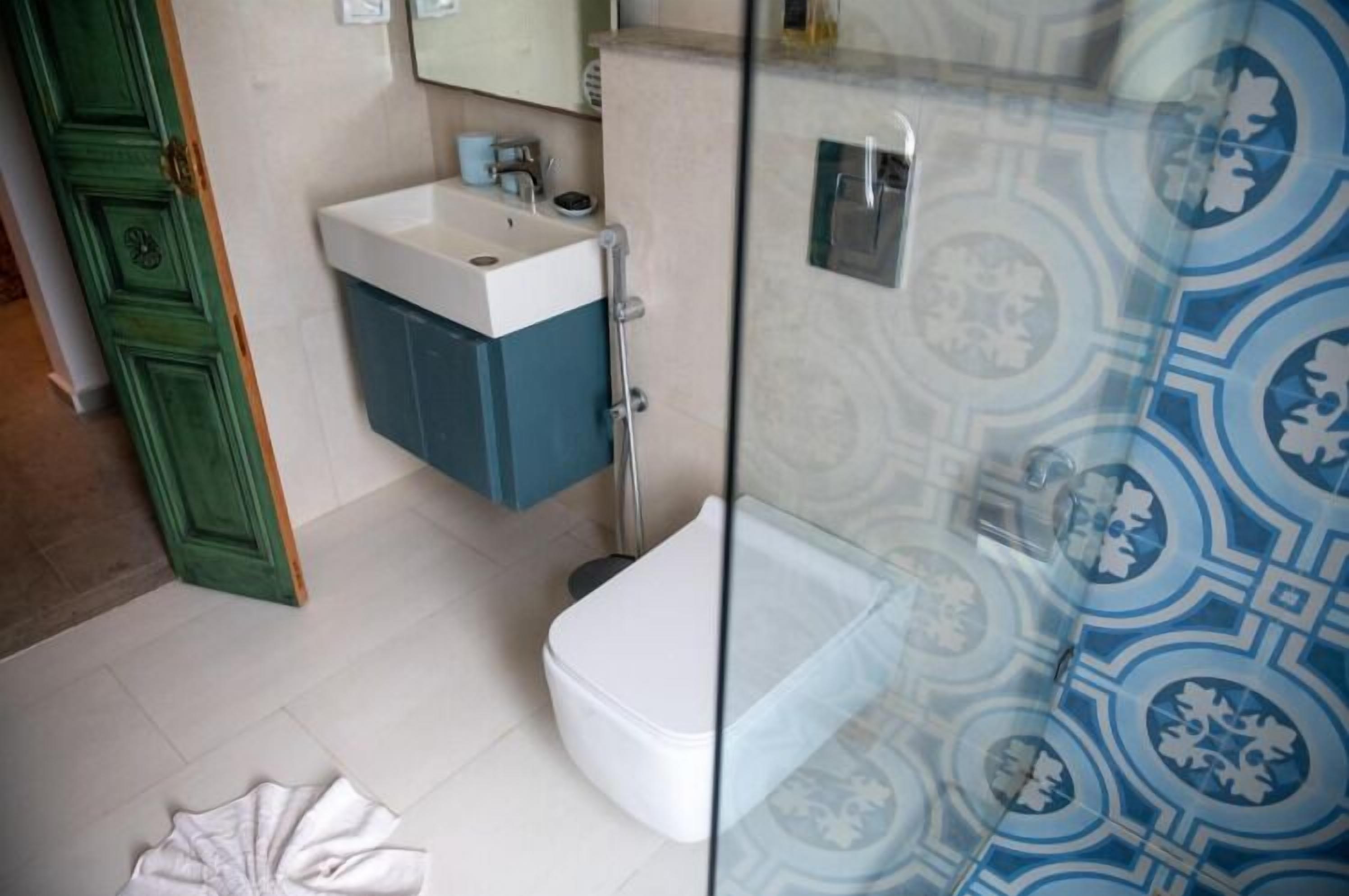 Une salle de bain avec des toilettes blanches, un meuble bleu et une cabine de douche en verre.
