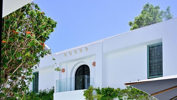 A modern pool area with a clear blue pool, white outdoor furniture, and a white building with green shutters. - Dar Gino - Maison d'hôtes (Kelibia)