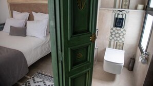 A bedroom with a bed, pillows, a green door, a toilet, and a patterned wall.