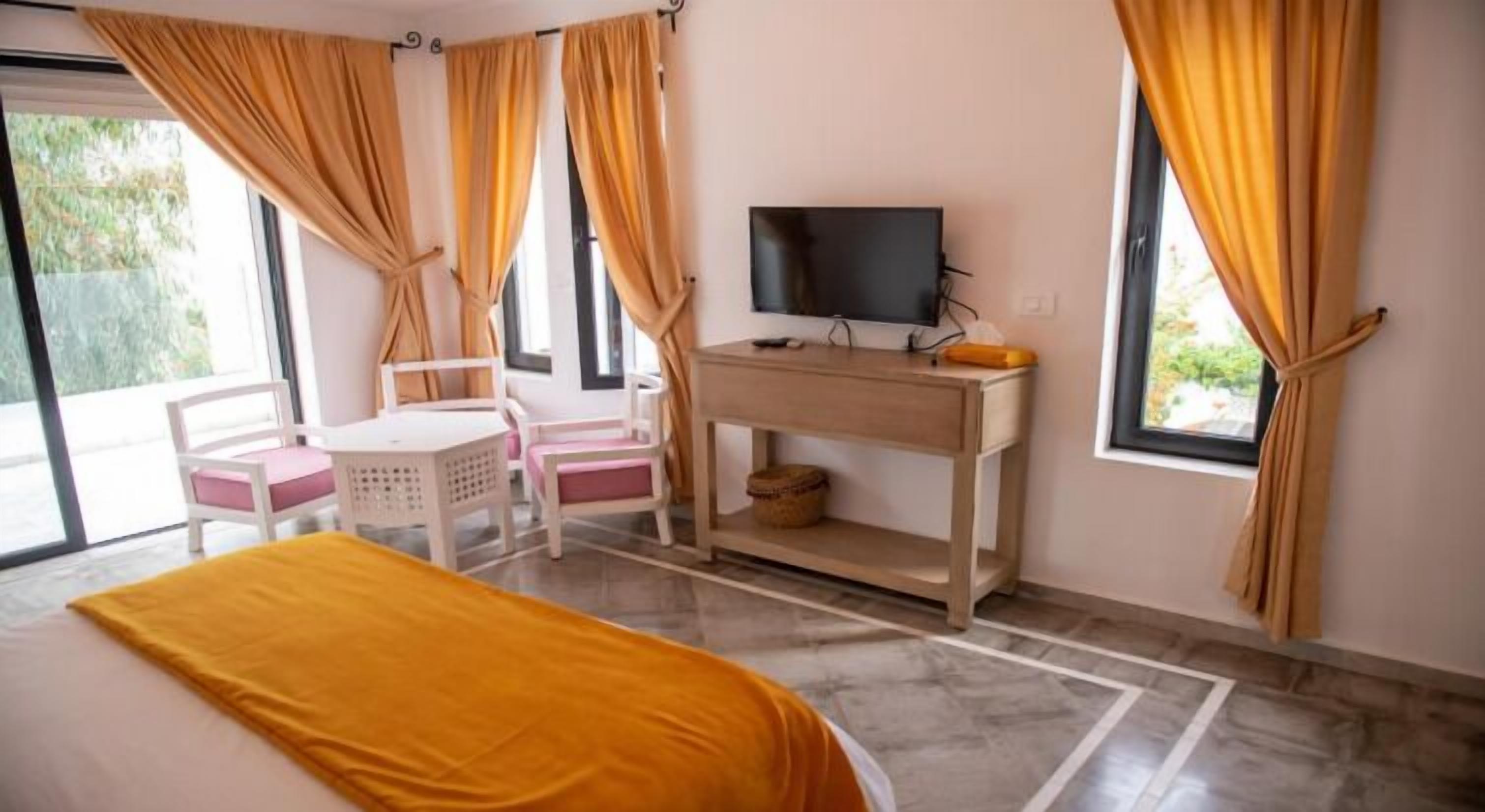 Una habitació d'hotel amb llit, escriptori amb televisió, cadira i finestra amb cortines.