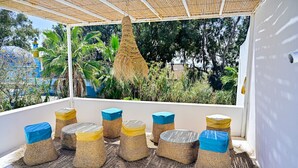 A covered outdoor seating area with woven furniture and a hanging basket. - Dar Gino - Maison d'hôtes (Kelibia)