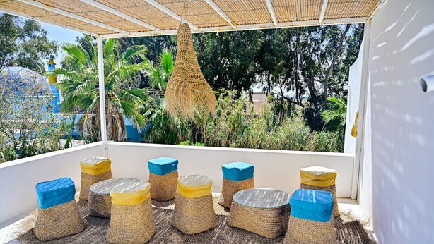 A covered outdoor seating area with woven furniture and a hanging basket.