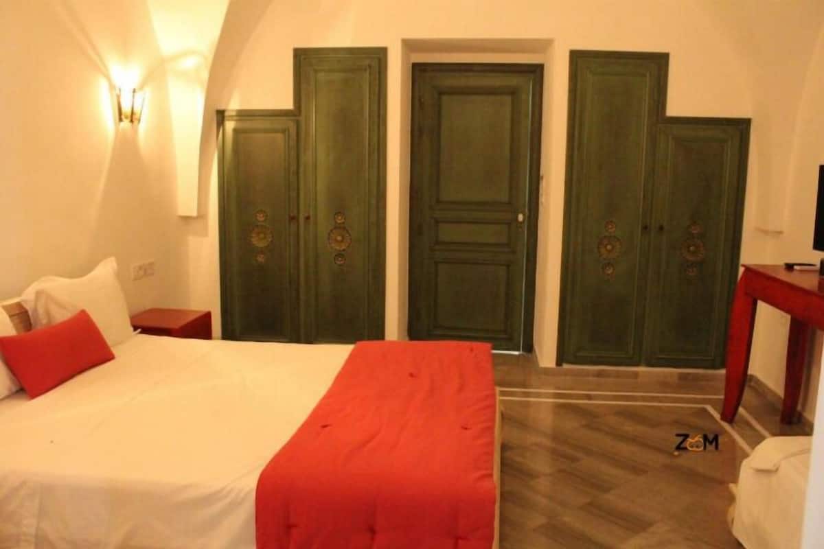 A bedroom with a bed, a red throw, two nightstands, a TV, and a wardrobe with three doors.