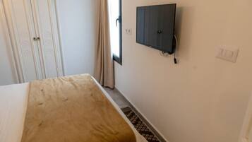 Una habitación con una cama, televisión montada en la pared, una puerta y un ventanal con cortinas.