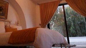 A bedroom with a bed, a chandelier, and large windows with curtains. - Dar Gino - Maison d'hôtes (Kelibia)