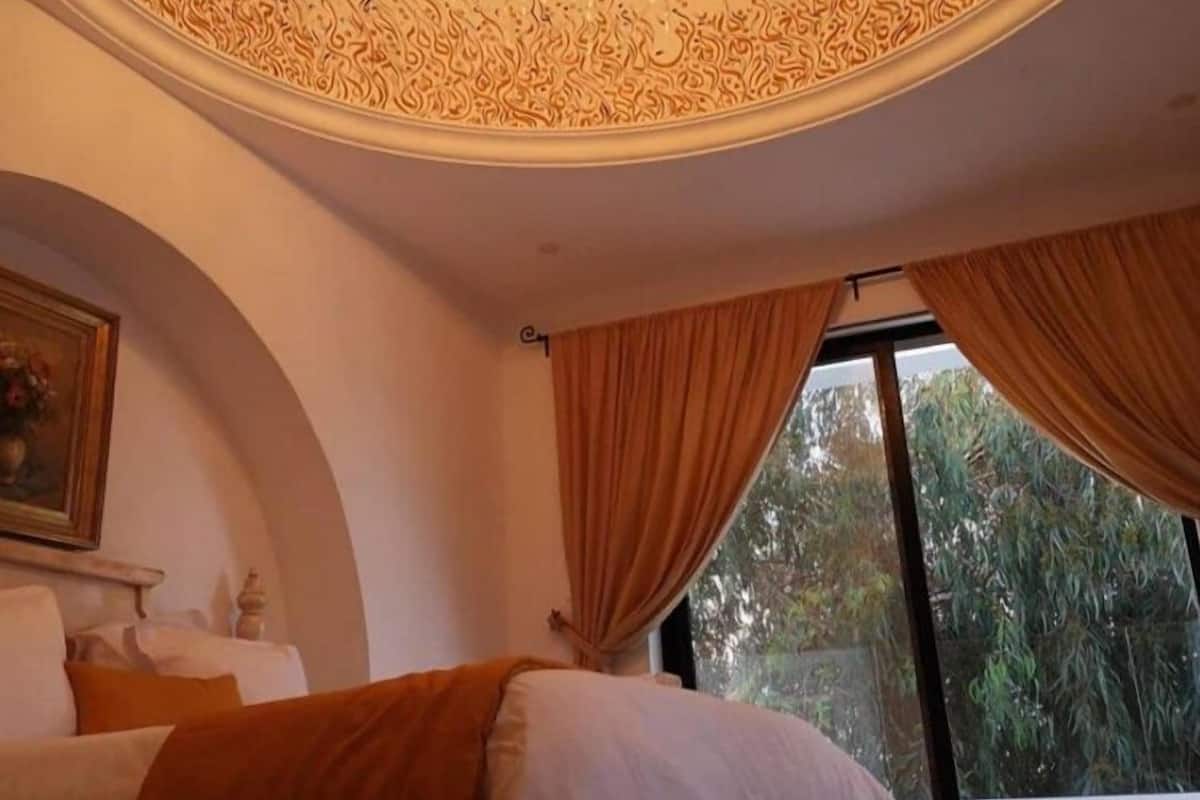 A bedroom with a bed, a chandelier, and large windows with curtains.