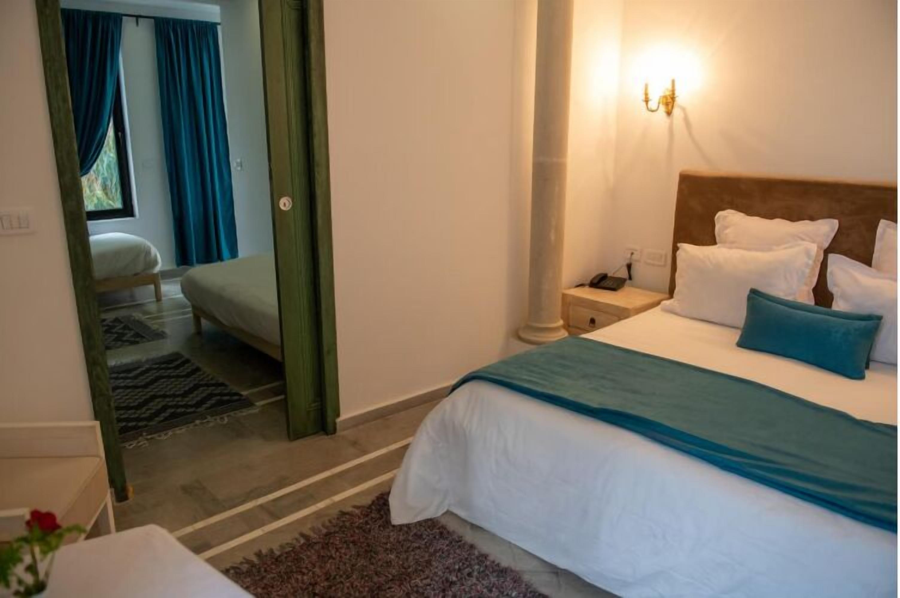 Un dormitorio con cama, mesita de noche, lámpara y vistas a una ventana con cortinas.