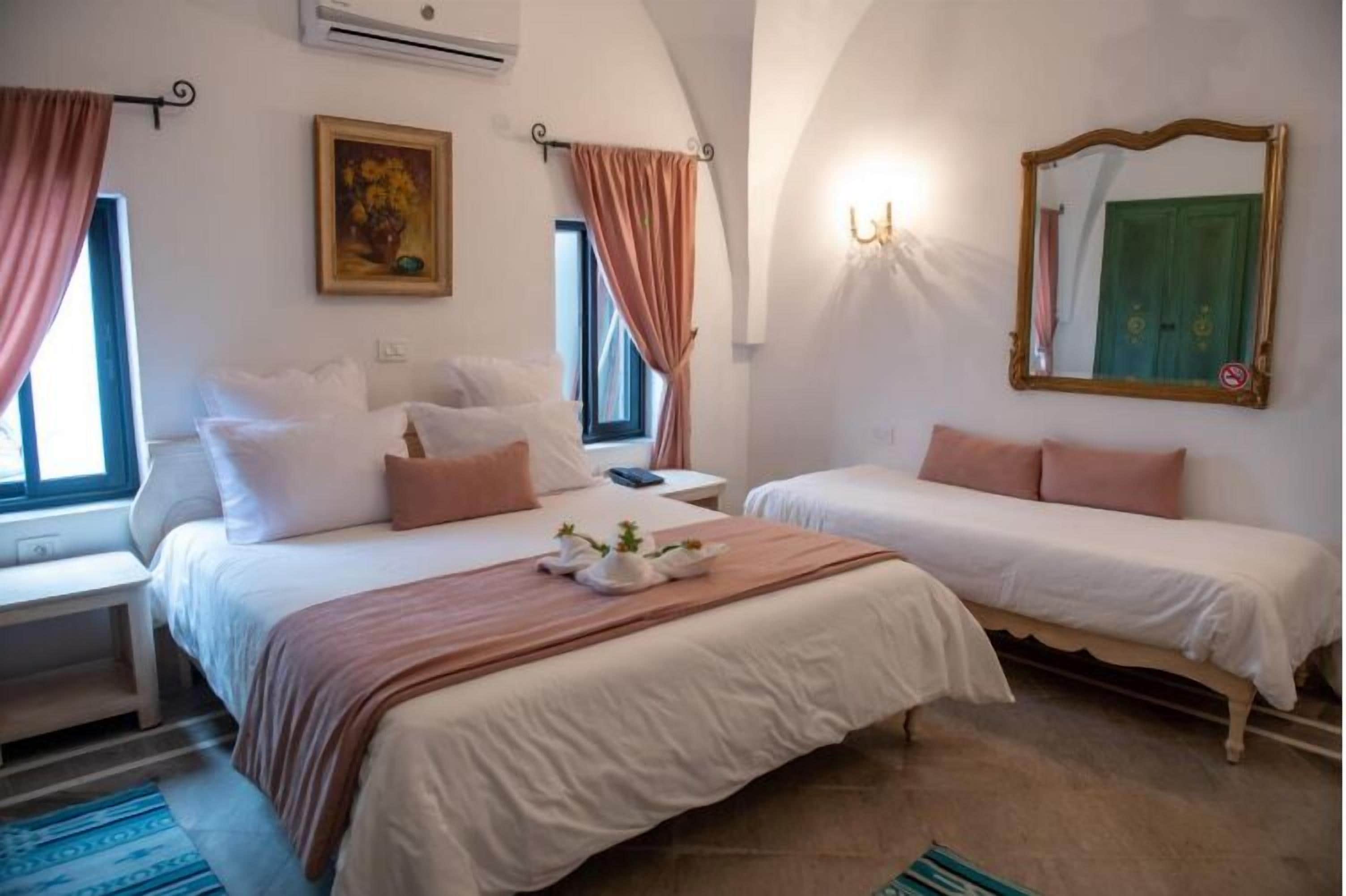 A hotel room with two beds, a painting, a mirror, and a window with curtains.