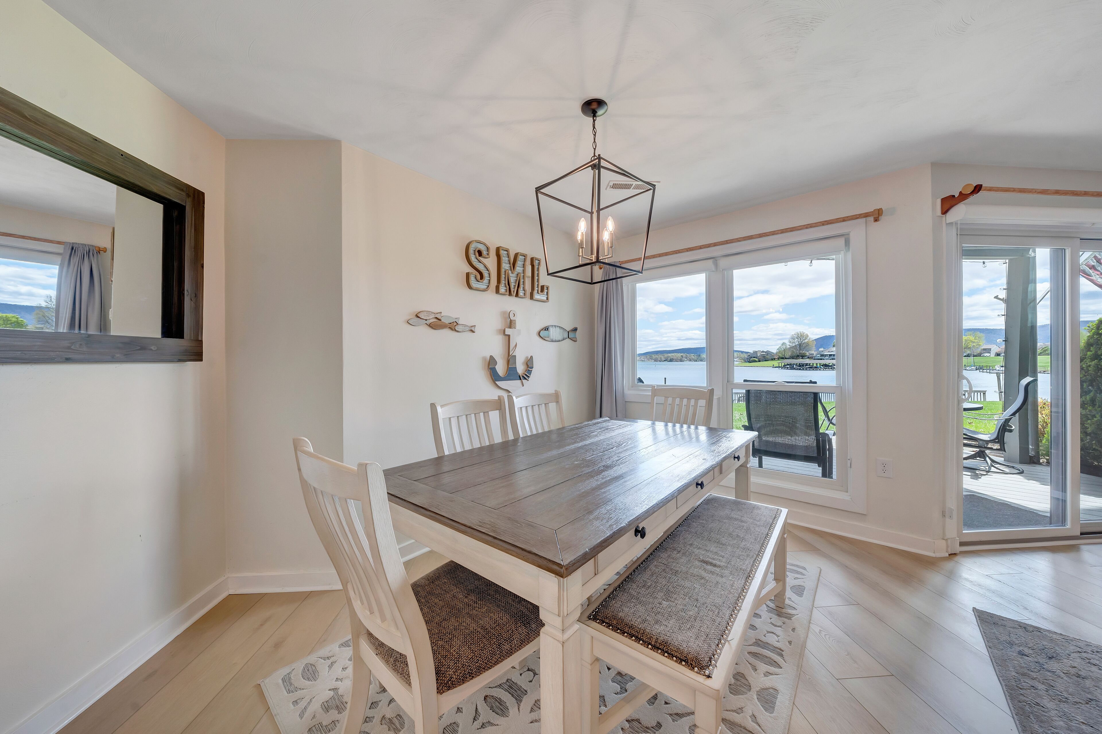 A dining area with a wooden table, white chairs, and a view through large sliding glass doors.