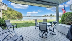 Eine überdachte Terrasse mit Tisch und Stühlen, mit Blick auf einen See und einen Steg.