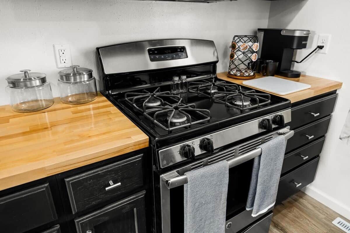 Een keuken met een fornuis, oven en koffiezetapparaat. Op het aanrecht staan twee glazen potten.