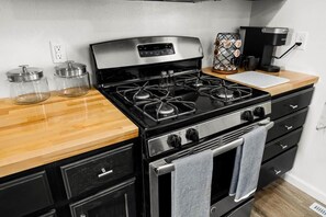A kitchen with a stove, oven, and coffee maker. There are two glass jars on the counter. - The Green Door-Cozy Stay by the Square Pubs & Cafe (Washington)