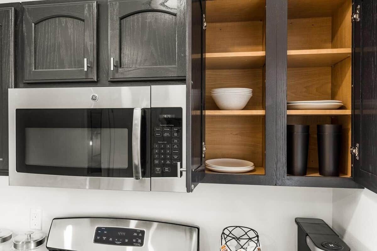 A kitchen with a built-in microwave and a wooden shelf cabinet.