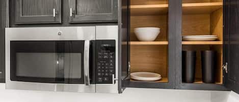 A kitchen with a built-in microwave and a wooden shelf cabinet.