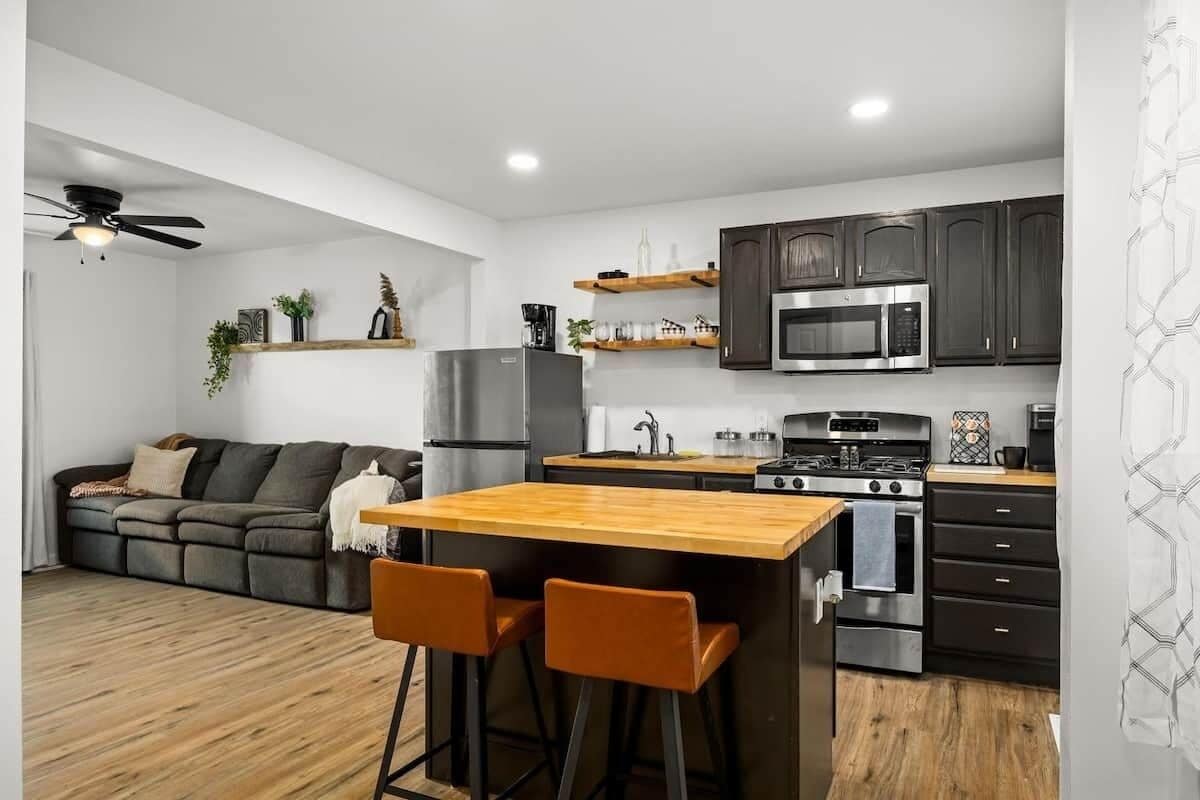 A modern kitchen with a central island, bar stools, a built-in oven, and dark cabinetry.