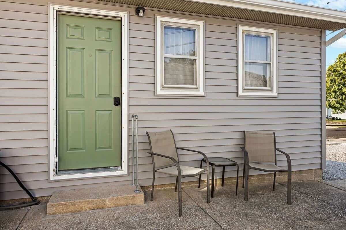 A house with a green door, two windows, and two chairs outside.
