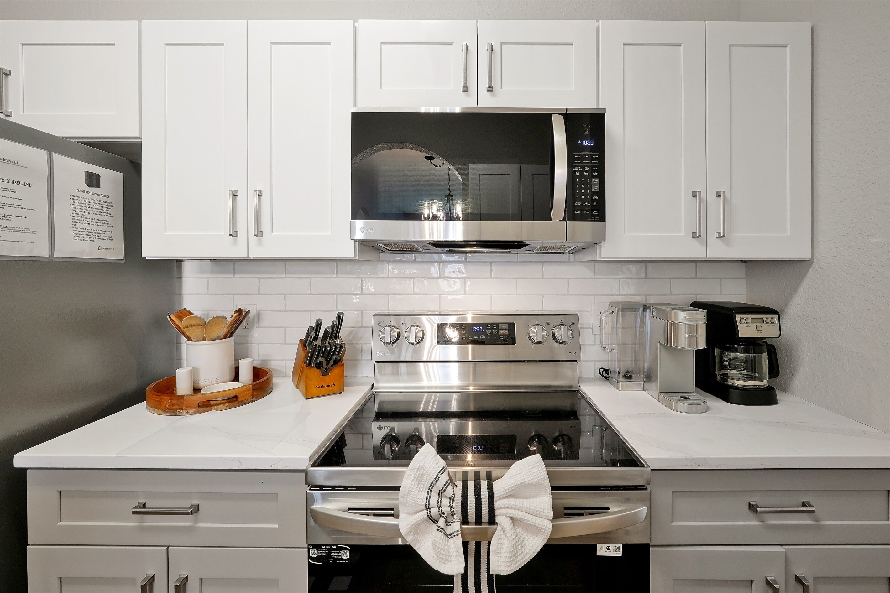 Una cocina con armarios blancos, un microondas de acero inoxidable, un horno y una cafetera.