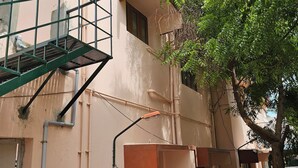 A building with a pink exterior, a green metal staircase, and a tree with green leaves. - Family Home in Prime Location close to City Center (Sathamangalam)