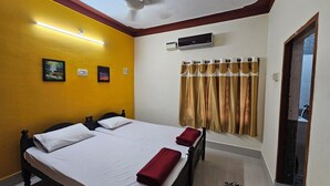 A hotel room with two beds, a ceiling fan, an air conditioning unit, and a window with curtains. - Family Home in Prime Location close to City Center (Sathamangalam)