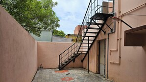 Une ruelle étroite avec un escalier en métal menant à une porte, le tout étant bordé de murs et doté d’un sol carrelé aux motifs hexagonaux.