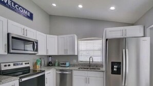 A modern kitchen with white cabinets, stainless steel appliances, and a welcome sign. - Pool home 5 miles to Disney! Great for families! (Kissimmee)