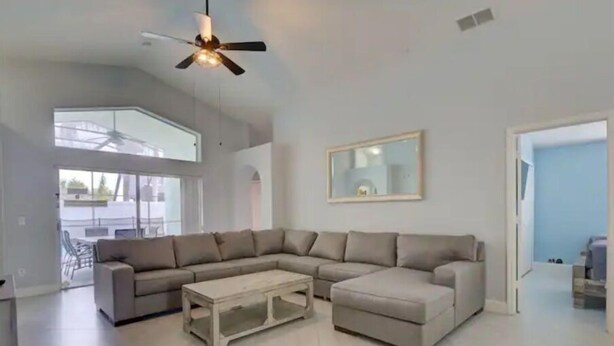 A spacious living room with a large L-shaped sectional sofa, a coffee table, and a ceiling fan. - Pool home 5 miles to Disney! Great for families! (Kissimmee)
