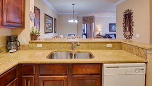 A kitchen with granite countertops, a double sink, wooden cabinets, a coffee maker, and a dishwasher. - Tuscana Resort Retreat (Kissimmee)