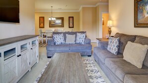 A living room with a gray sofa, a wooden coffee table, and a TV on the wall. - Tuscana Resort Retreat (Kissimmee)