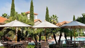 A poolside area with outdoor seating and umbrellas. - Tuscana Resort Retreat (Kissimmee)