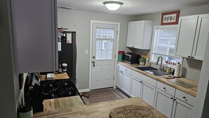 Una cocina compacta con gabinetes blancos, una encimera de madera, una estufa y un lavamanos.