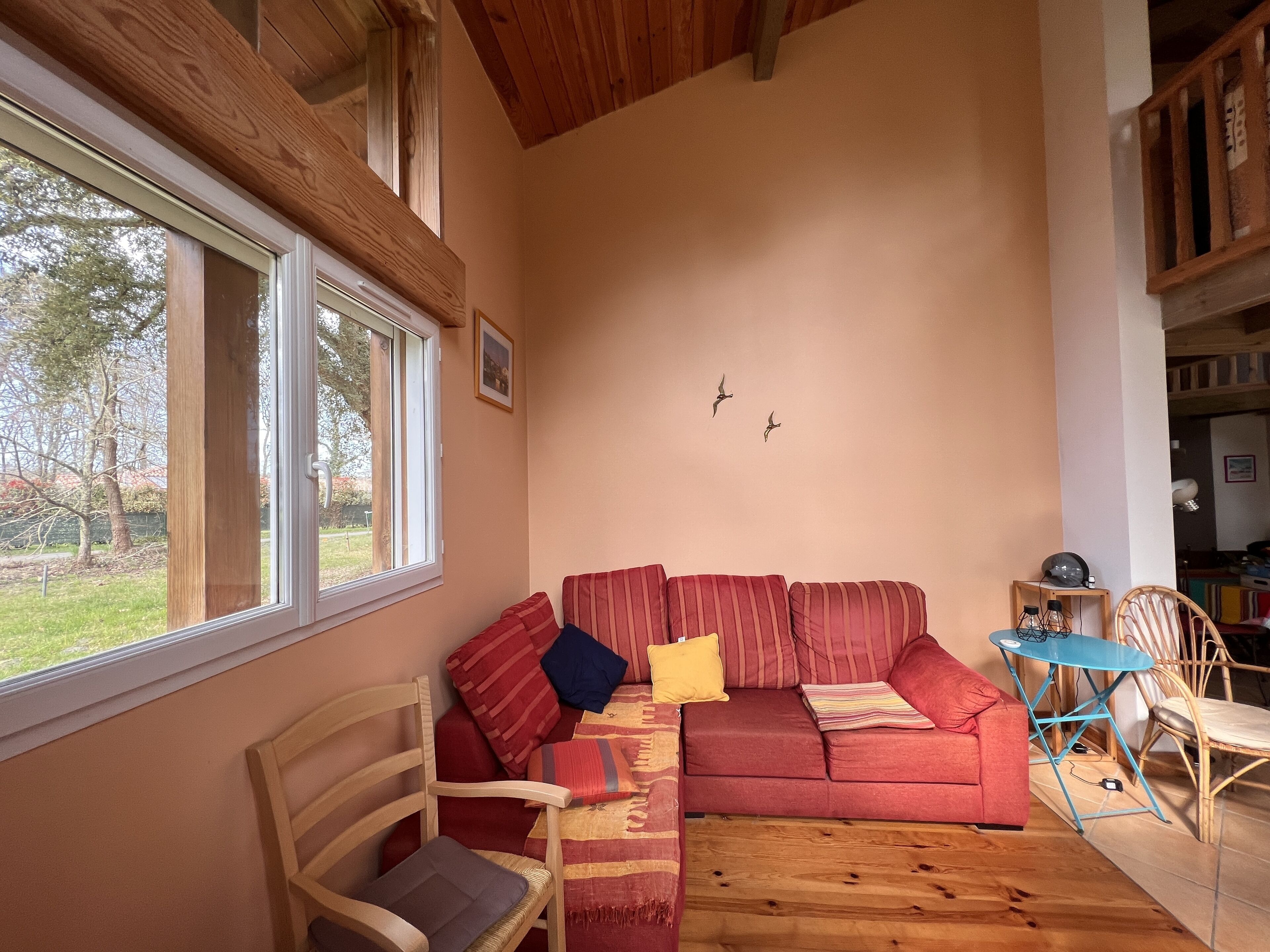 Una sala de estar acogedora con un sofá rojo, sillas de madera, una mesita y un ventanal con vistas a árboles.