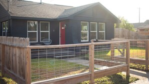 Une maison à deux étages, à l’extérieur sombre, avec une porte rouge et un jardin clôturé à l’avant.