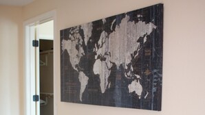Une pièce avec un bureau en verre, une chaise grise, une carte du monde accrochée au mur et une étagère blanche.