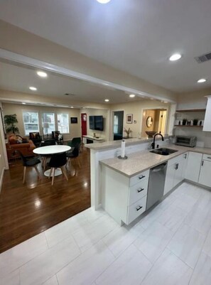 A modern kitchen with white cabinetry, a central island, and a dining area with a round table and chairs. - Gorgeous Renovated Historic Home. (Houston)