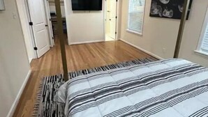 Une chambre à coucher avec un lit, un téléviseur fixé au mur, une porte et une fenêtre avec des stores.